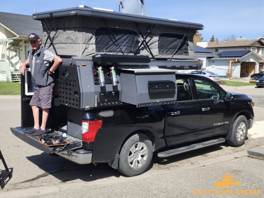 A man standing on the back of a truck-bed camper.