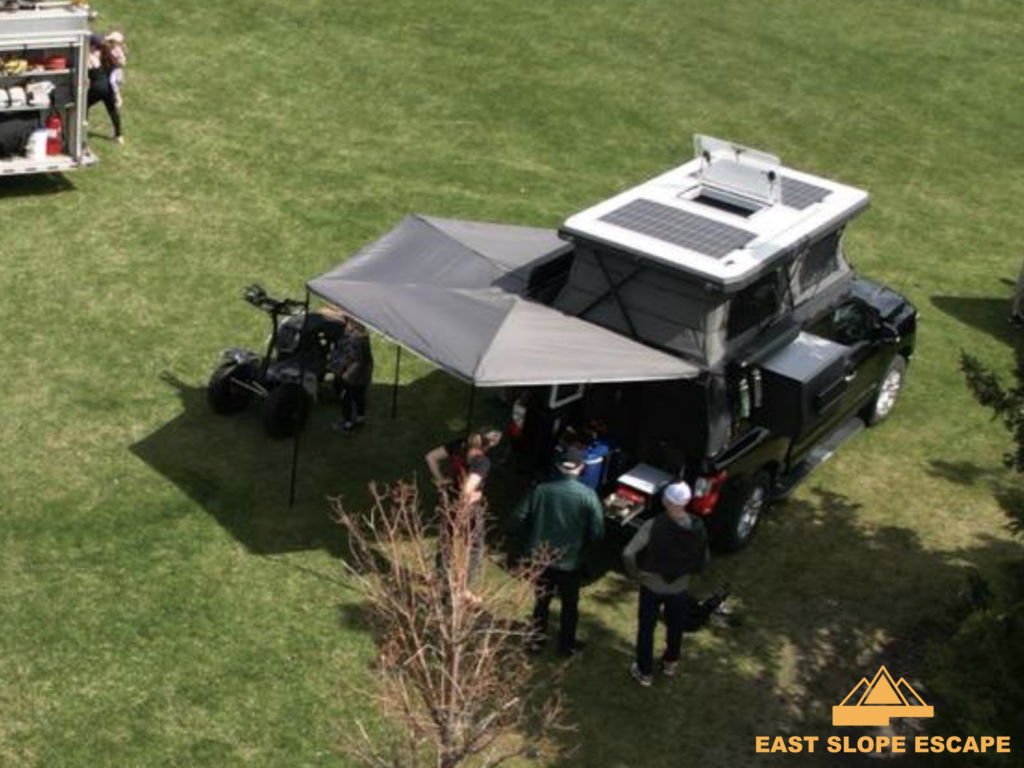 This is a drone shot of a camper. You can see the rooftop and extension of the camper and a few people gathered around.